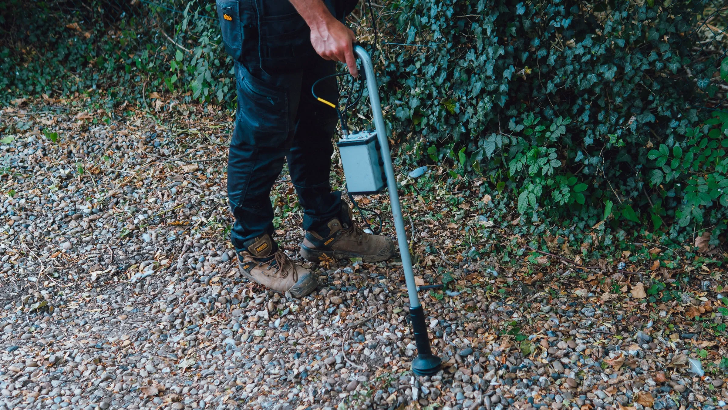 Engineer holding an acoustic ground microphone on a stand against a gravel drive