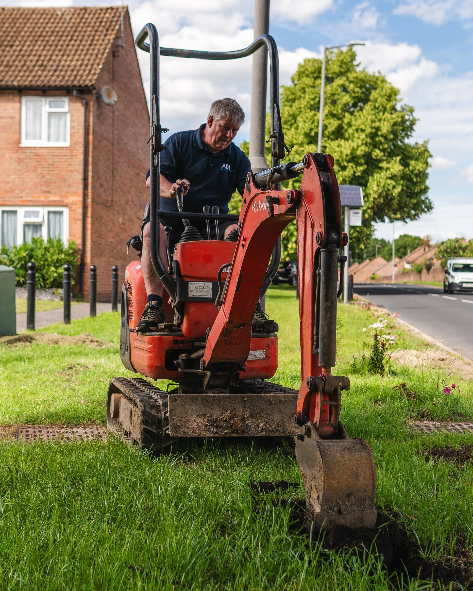ADI engineer operating a mini digger on a grass verge beside a residential street