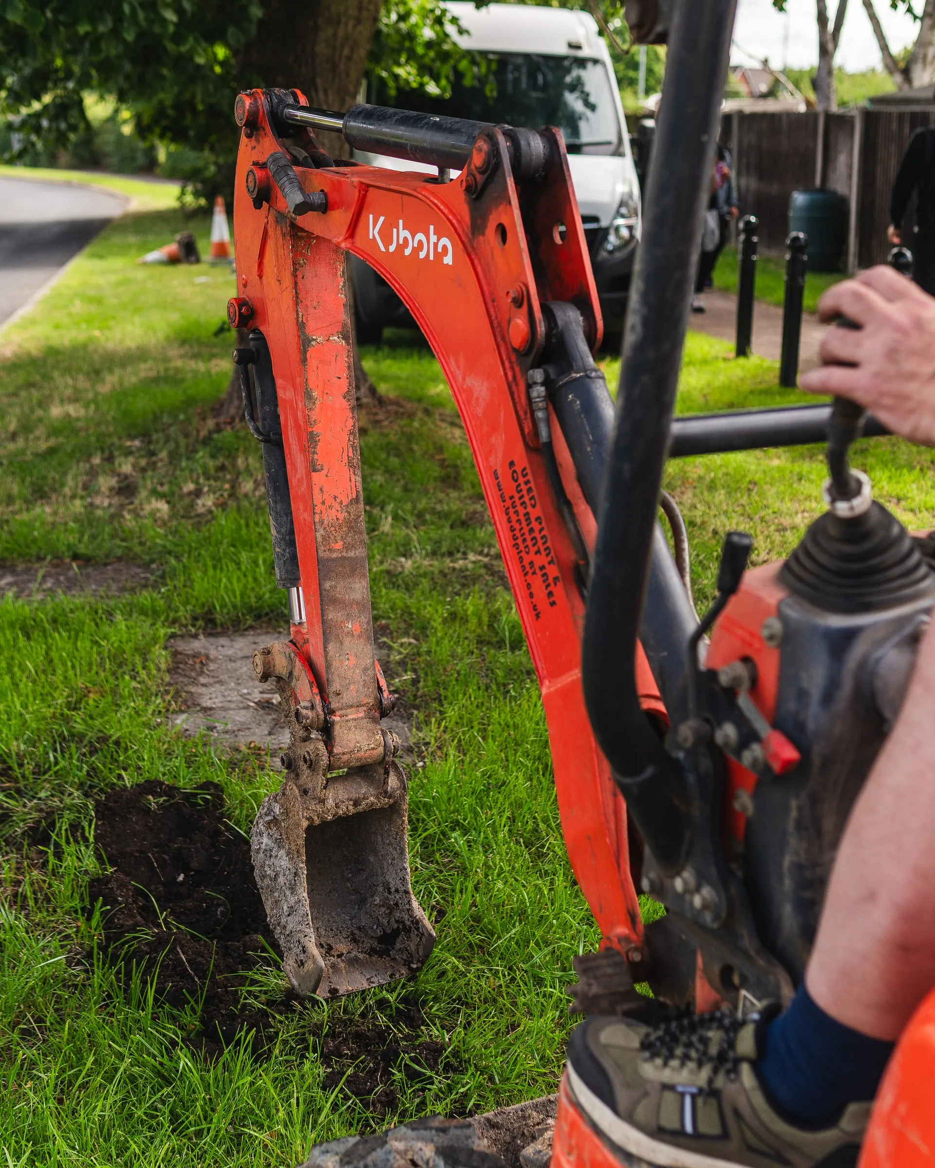 Mini digger bucket over a small, neat trench cut into a grass verge