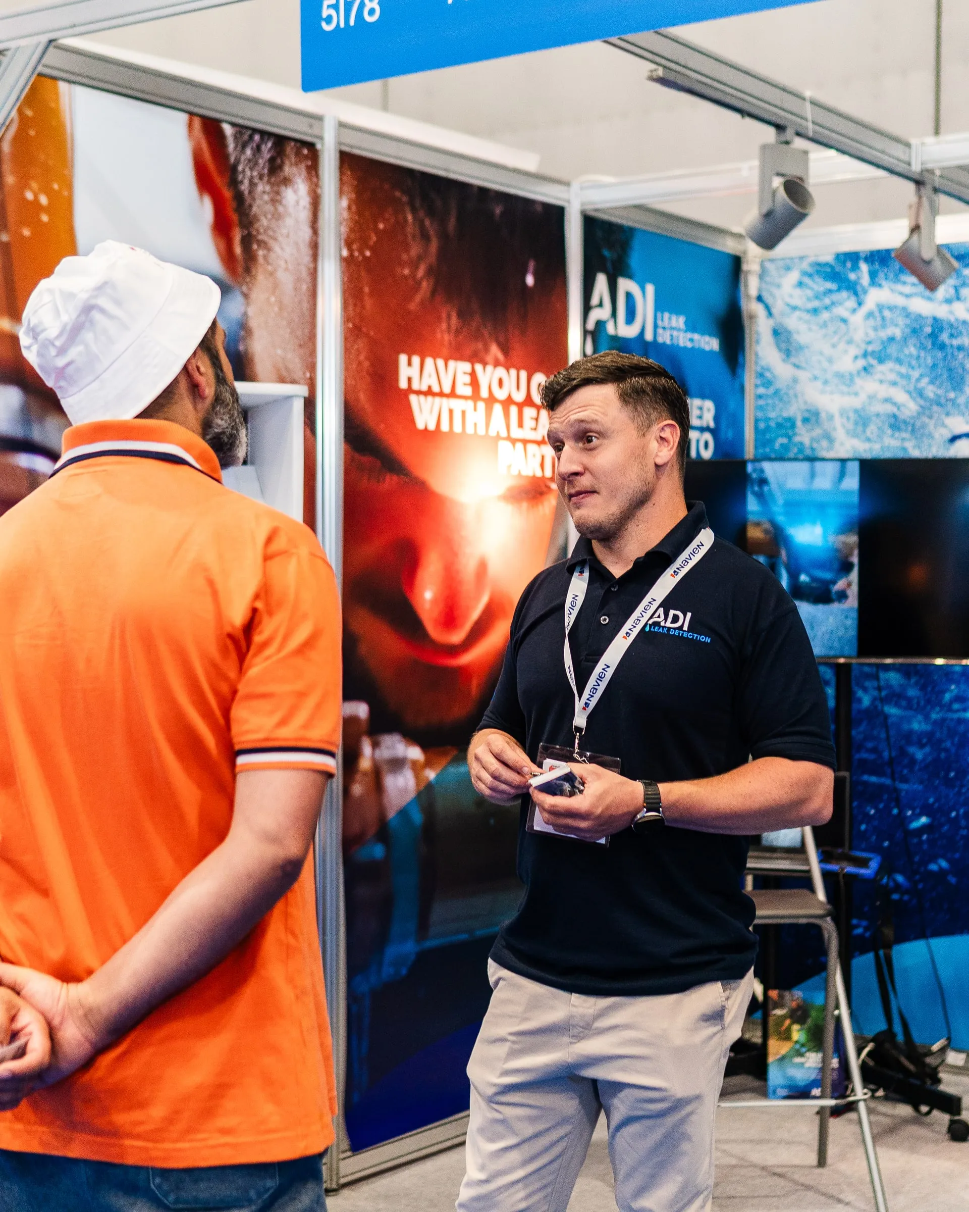 ADI team member in a branded polo shirt talking with a visitor at ADI’s trade show stand
